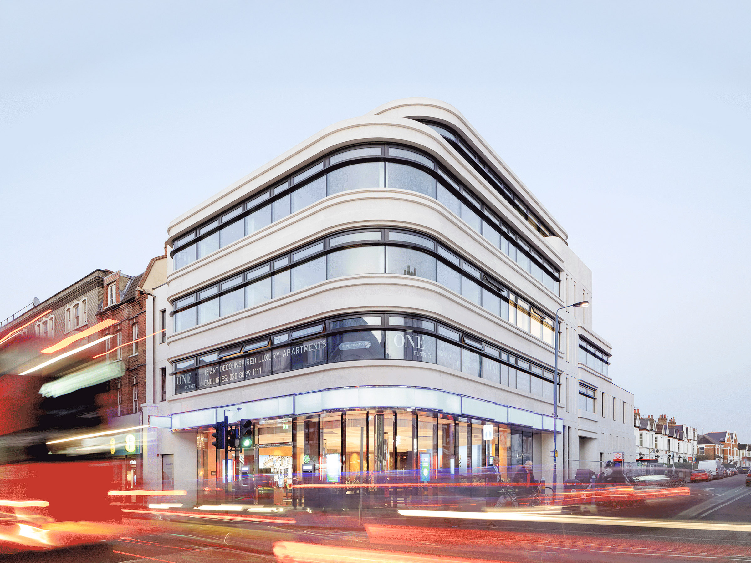 Twilight street view showing the building’s curved edge illuminated within the city context, framed by motion blur.