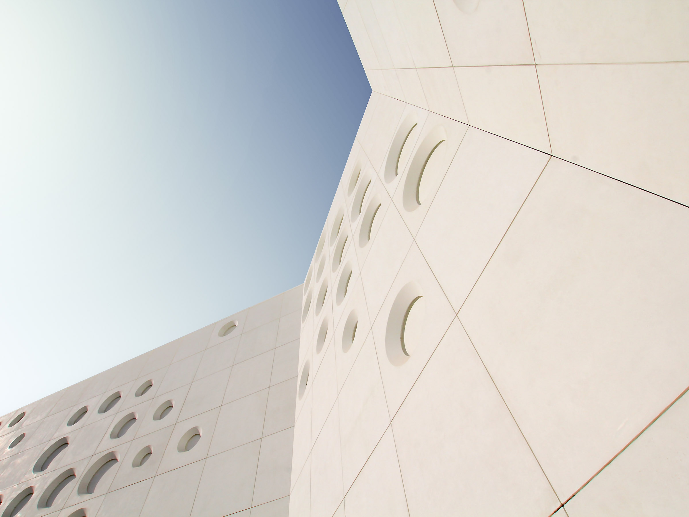 Oblique view of the façade showing deep circular recesses casting shadows across 3 m by 3 m GRC panels.