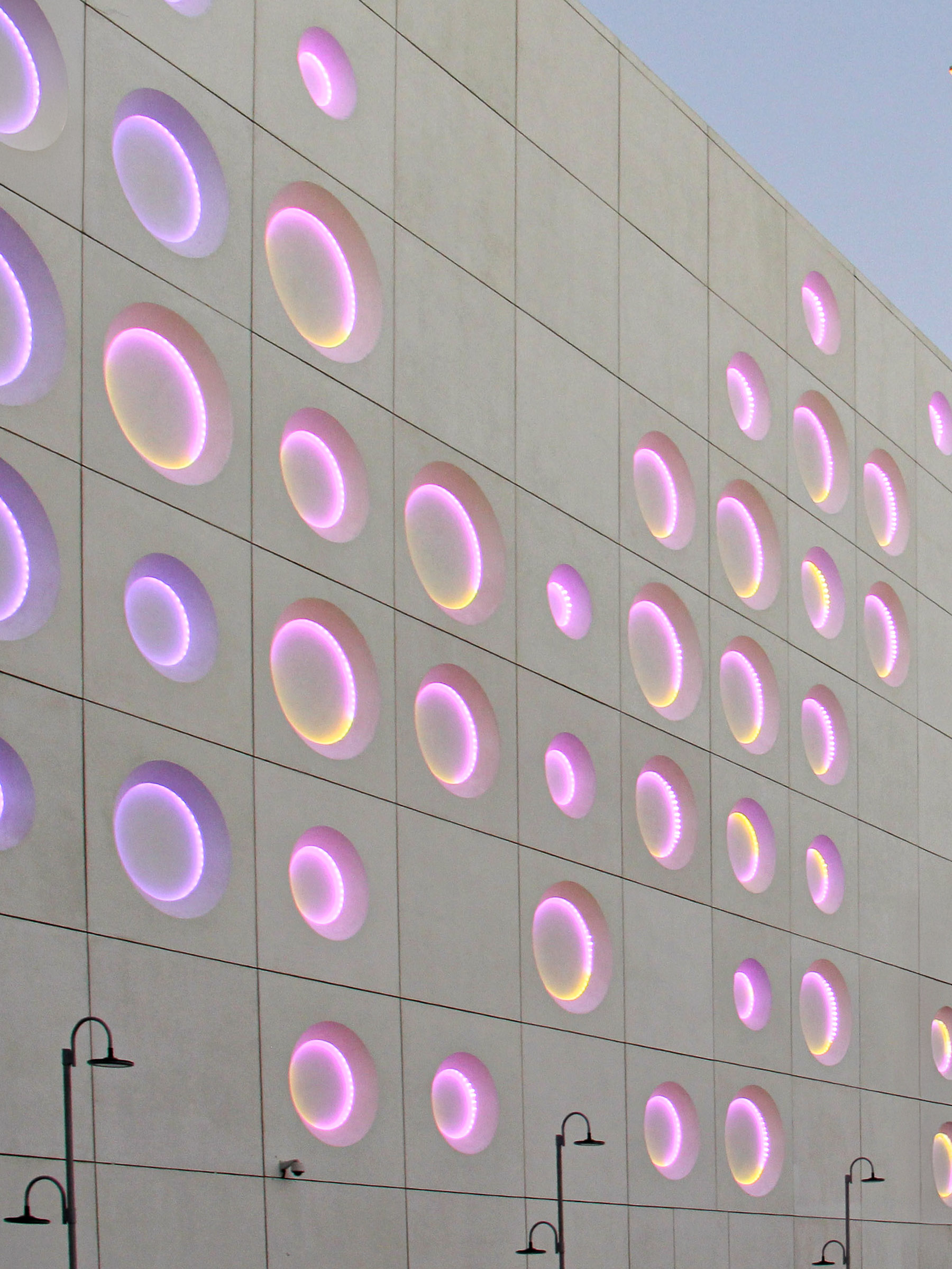 Façade at dusk illuminated with purple lighting, showing rhythmic pattern and surface depth across the building.