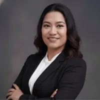 Professional woman in black blazer and white shirt against gray background, arms crossed