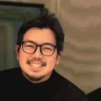 A smiling man with black hair and glasses wearing a black shirt