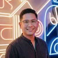 Smiling man with glasses in front of colorful neon signs