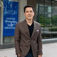 Man in brown blazer standing outdoors in front of blue storefront sign