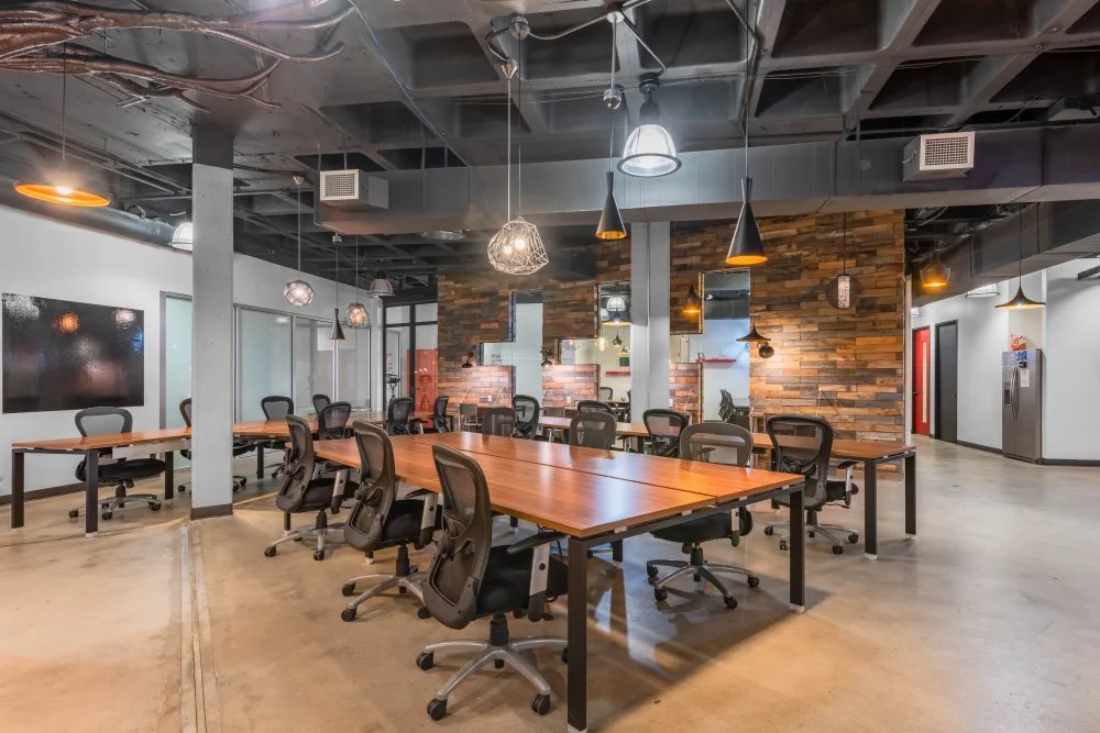 Modern office space with wooden tables, black mesh chairs, and pendant lighting fixtures.