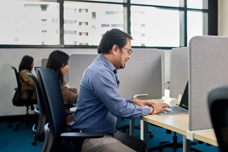 Man working at computer in modern office with colleagues at desks behind