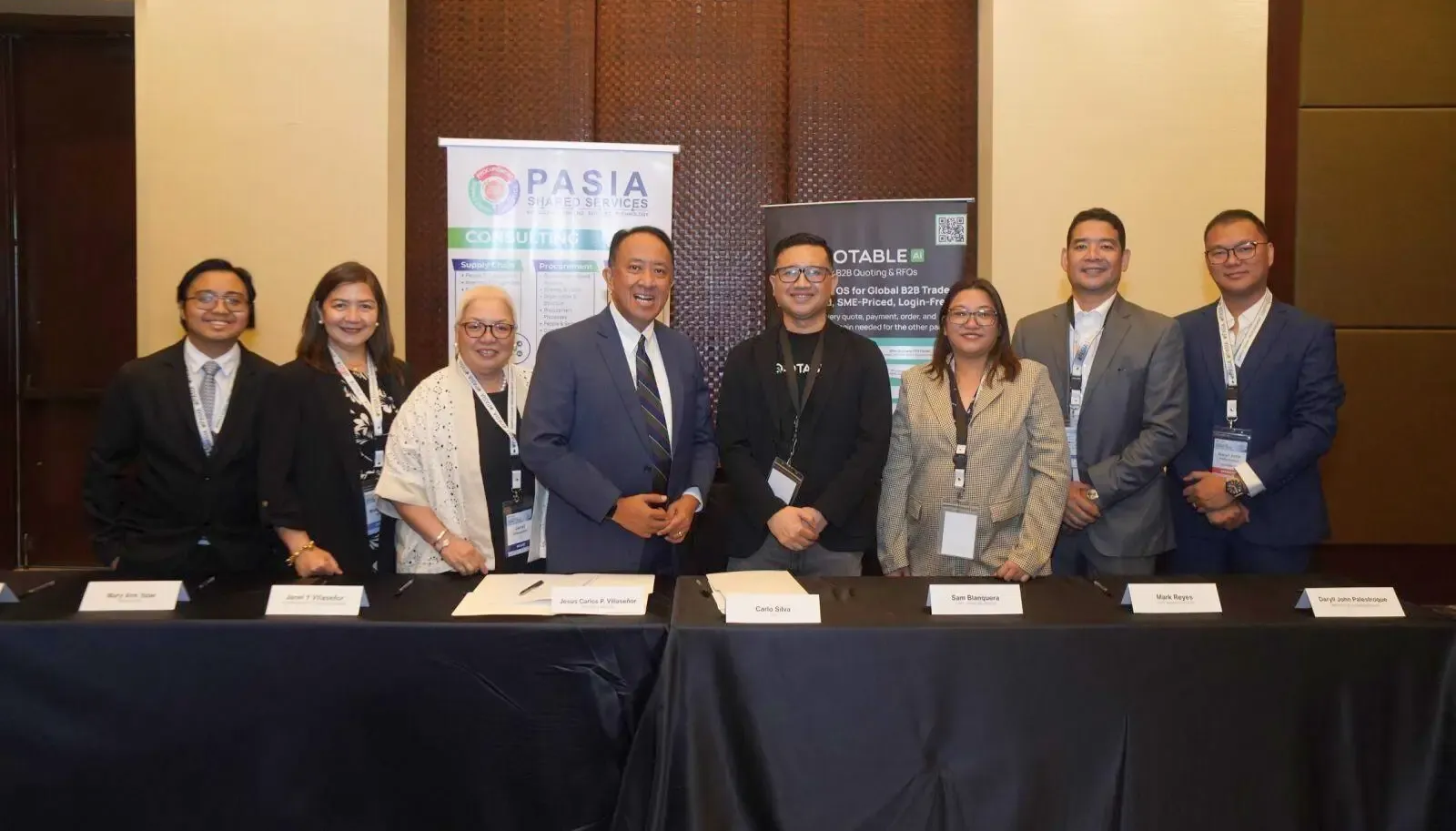 Eight business professionals posing together at a conference panel with PASIA and QUOTABLE banners displayed