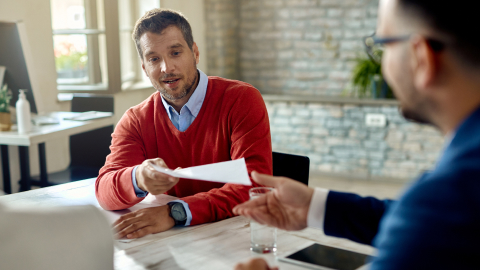 Business advisor handing multi-currency account paperwork across a desk to a client.