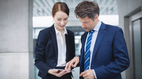 Two professionals reviewing account opening requirements on a tablet in an office lobby.