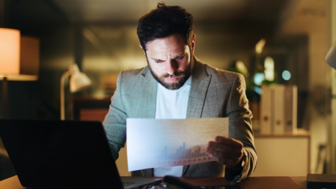 Finance manager examining a printed statement by laptop light in a dim office.
