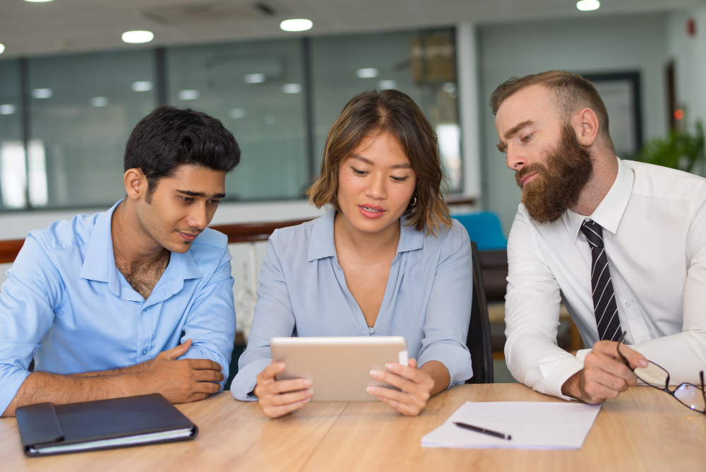 Three colleagues reviewing FX cost figures on printed reports in a meeting.