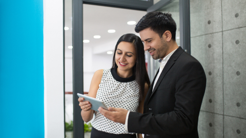 Two colleagues reviewing multi-currency account options on a tablet in an office corridor.