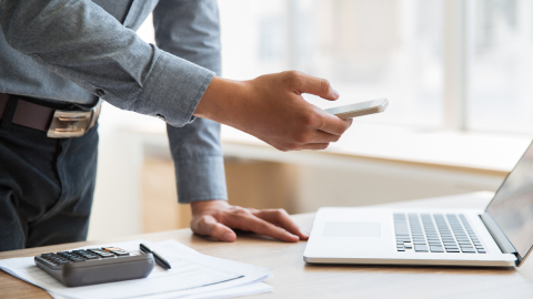 Business owner checking a phone beside a calculator and laptop while reviewing wire fees.