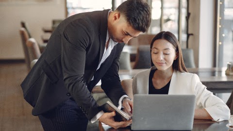 Manager showing a colleague quote-to-cash pricing options on a tablet beside a laptop.