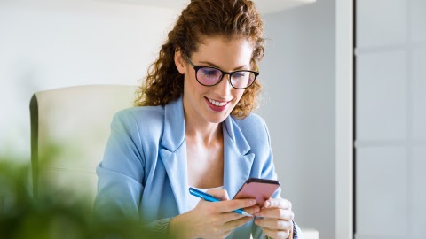 Business owner reviewing an invoice approval on her phone at a bright office desk.