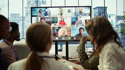 Team joins a video call with international colleagues on a large screen.
