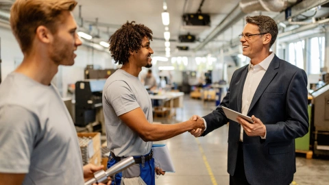 Business consultant shakes hands with factory workers on a production floor.