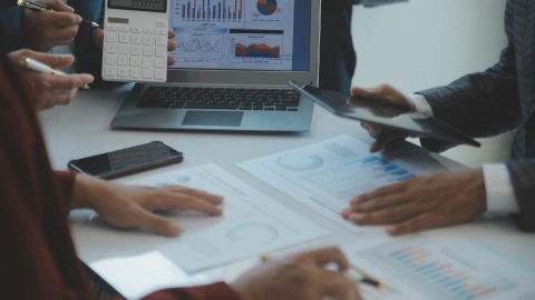 Team reviews spending charts and reports with a calculator at a conference table.