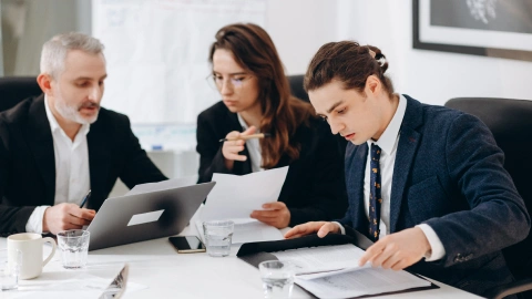 Finance team reviews documents and a laptop during a conference room meeting