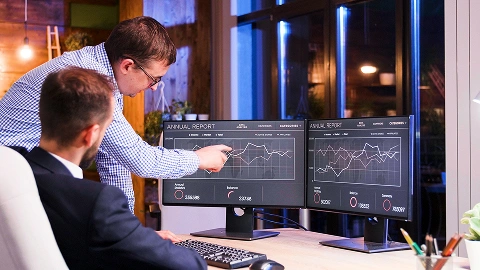 Two analysts compare financial dashboards side by side on dual monitors