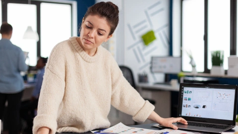 Businesswoman compares software options on a laptop while checking printed notes
