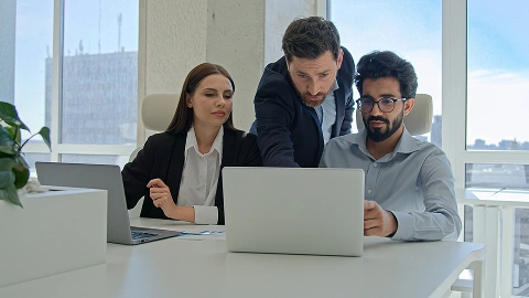 Three coworkers look at a laptop screen with concerned expressions