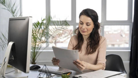 Businesswoman reviewing paperwork at her desk in a bright office.