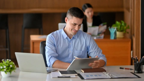Businessman reviewing notes on a tablet at his desk.