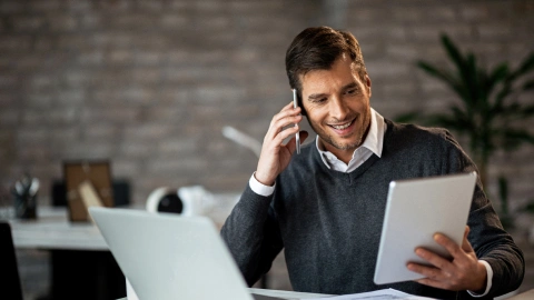 Man smiling on a phone call while holding a tablet.