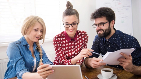 Three colleagues reviewing a tablet together at a table.