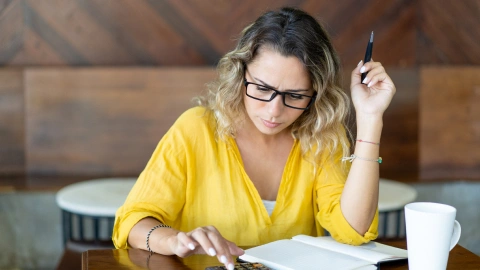 Woman writing in a notebook at a café-style table.
