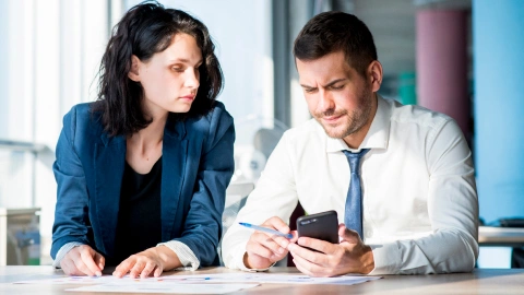 Two colleagues reviewing a phone together over paperwork.