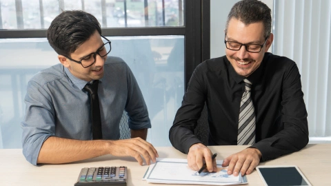 Two businessmen reviewing documents together with a calculator.
