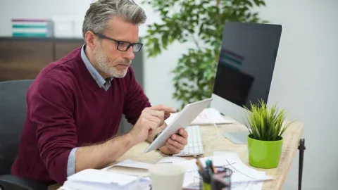 Man using a tablet at his desk beside a desktop computer.