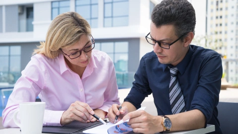 Two colleagues reviewing a document together outdoors.