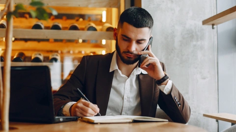 Remote worker takes a call and writes notes while working from a café