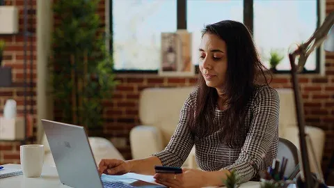 Woman working on a laptop while checking her phone in an office.