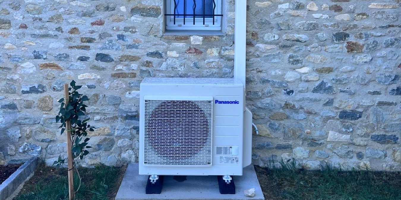 Groupe extérieur Panasonic Etherea posé sur dalle contre un mur en pierres à Rochebaudin