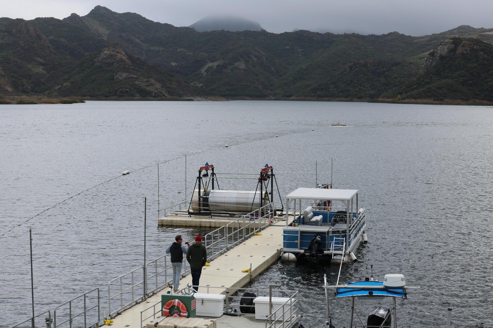Two men walk on a dock toward a prototype desalination pod that is being tested in a reservoir.