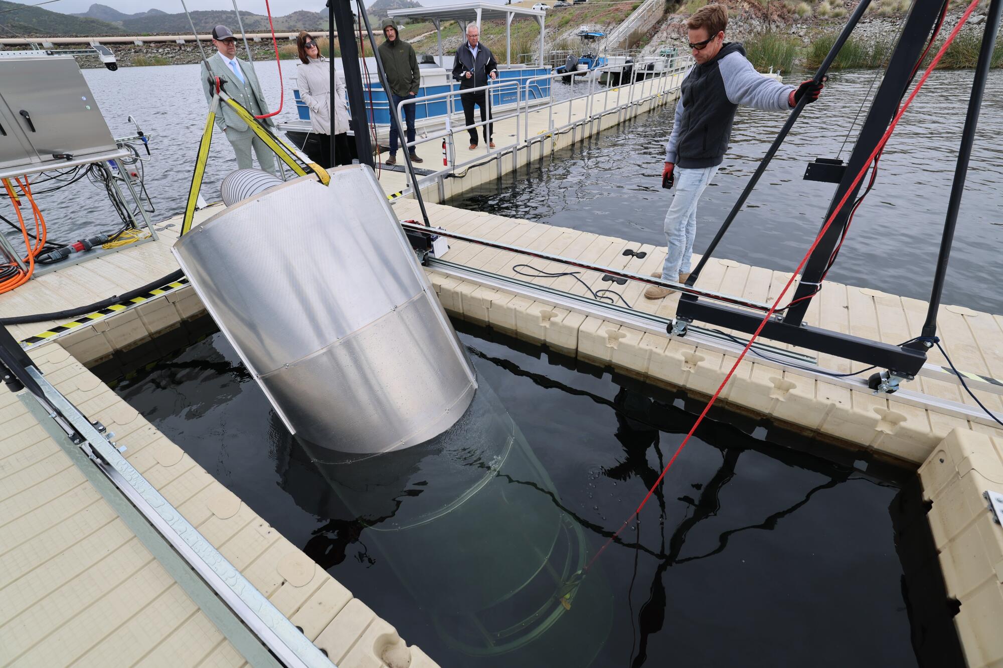 A man watches as a cylindrical prototype is lowered into a reservoir.