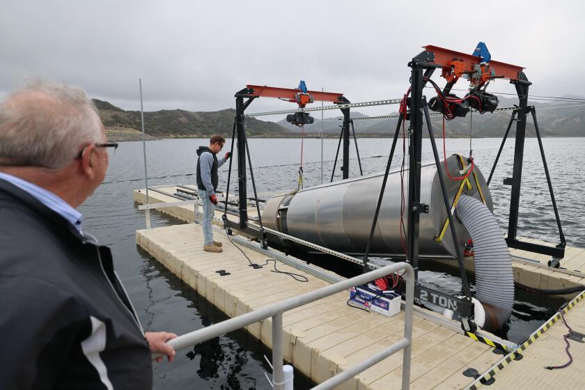 Westlake Village, CA - March 12: Dr. Tim Quinn, left, water policy strategist, OceanWell, watches Mark Golay, director of engineering projects at OceanWell, lower a water cleaning/desalination pod that is being tested at the Las Virgenes Reservoir in Westlake Village Wednesday, March 12, 2025. The company's plan, once the pod has been tested, is to deploy a "farm" of them on the ocean floor near Malibu. The water district that supplies Calabasas, Agoura Hills and other L.A. suburbs is working with a company to pioneer a new desalination technology, testing a system of filtration pods that will be anchored to the ocean floor at depths of more than 1,000 feet. Las Virgenes Municipal Water District, which now relies entirely on water from Northern California, says the desalination pods that the company OceanWell plans to deploy off the coast will help boost local supplies and reduce dependence on imported water, without causing the environmental harm that are a large desalination plant on the coast would. The company has started testing the system at Las Virgenes Reservoir. Water managers are hoping this type of desalination technology will help the area become less vulnerable to drought. (Allen J. Schaben / Los Angeles Times)