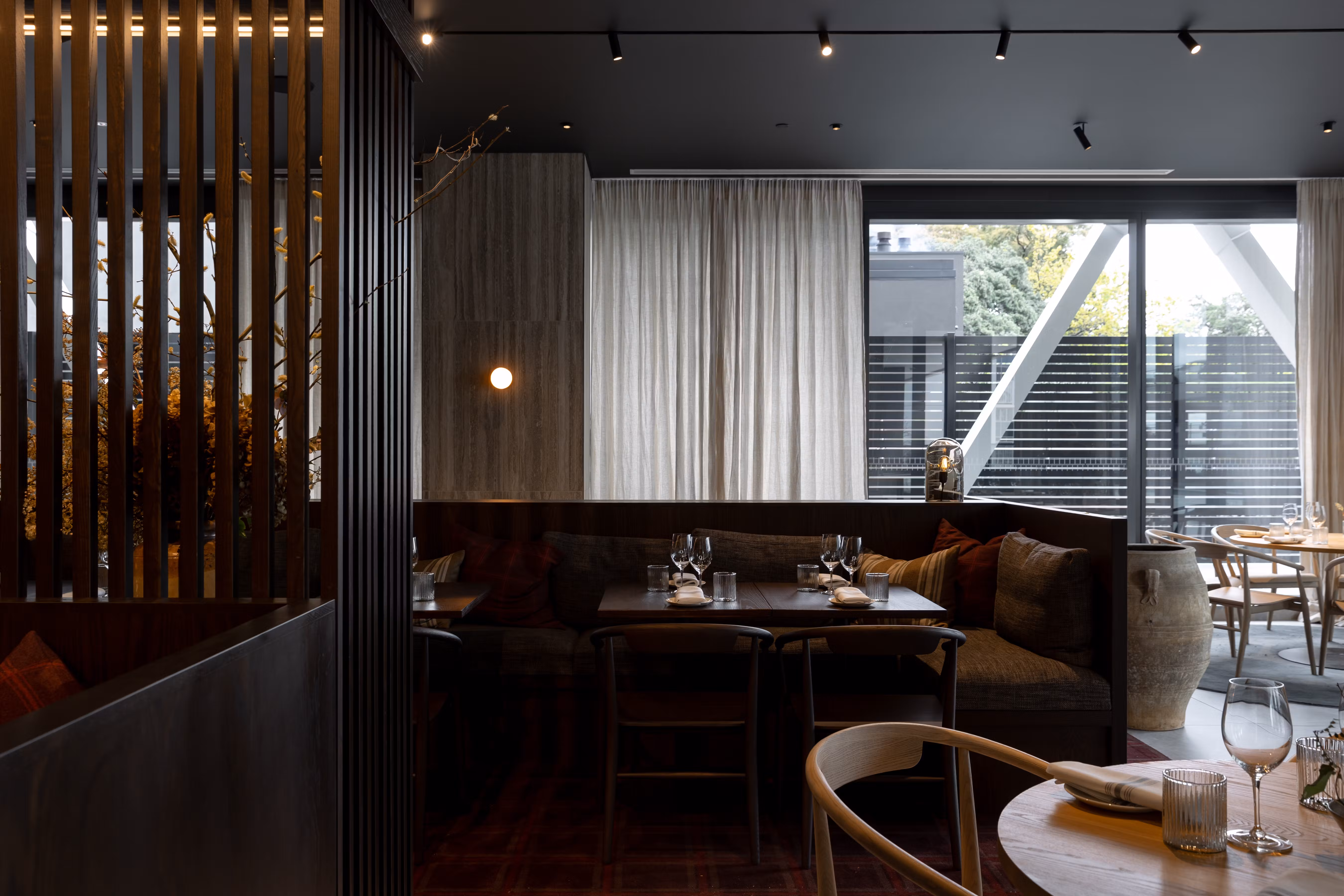 Cozy restaurant interior with dark wooden booths, tables set with glassware, and large windows with white curtains.