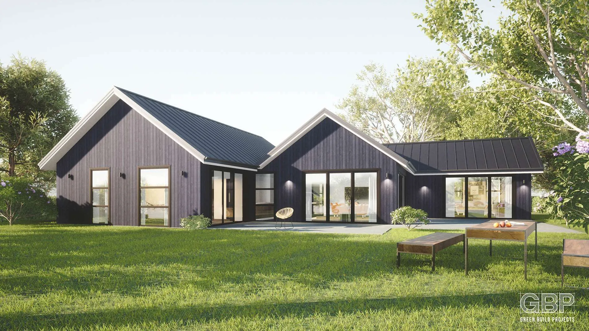 Modern single-story house with black exterior, large windows, and patio furniture on a green lawn surrounded by trees.