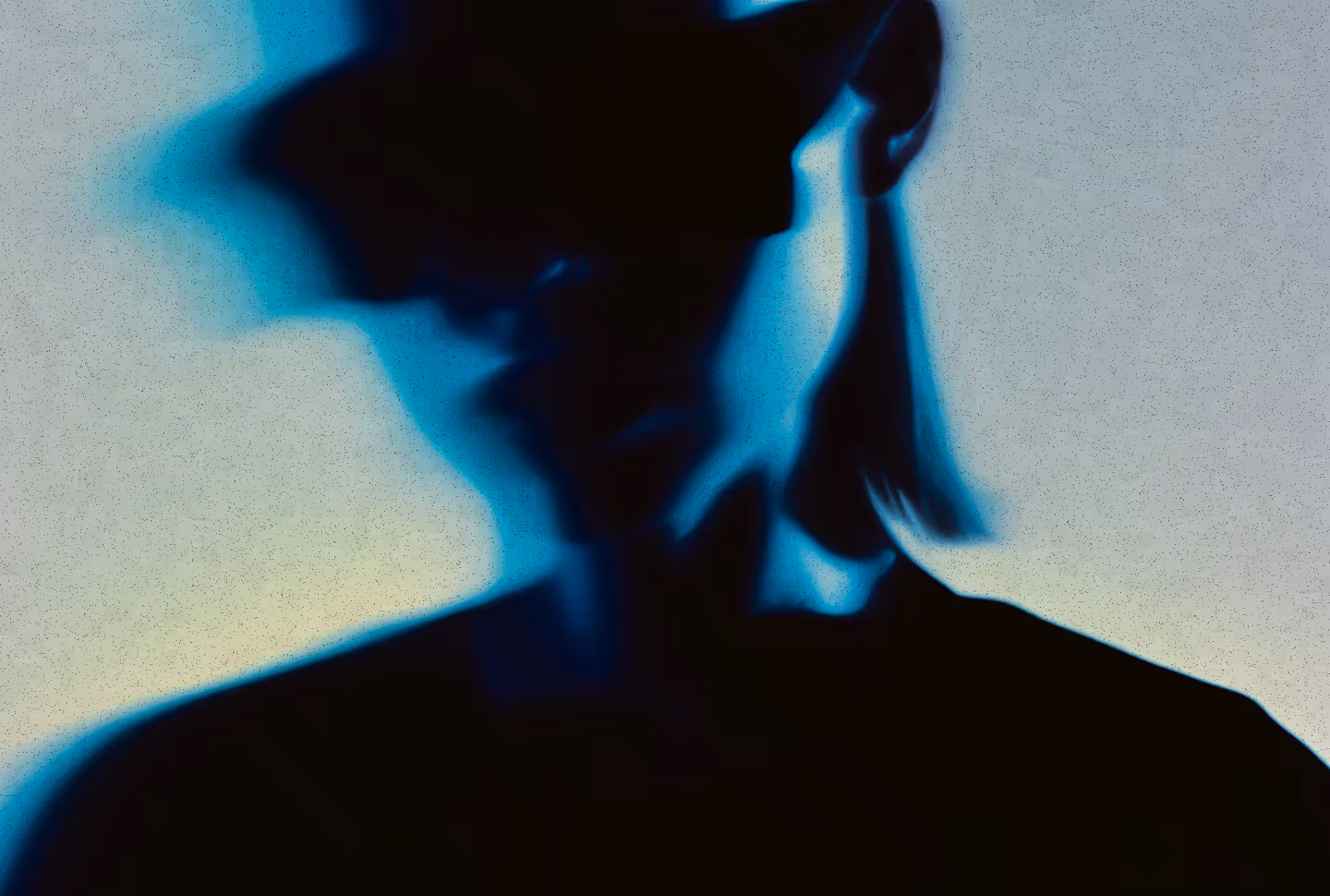 Silhouette of a person with short hair tied back, blurred with blue light effects.