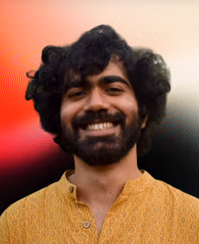 Smiling man with curly black hair and beard wearing a patterned yellow shirt against a gradient background.