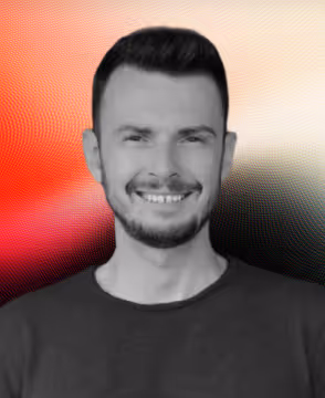 Smiling man with short dark hair and beard wearing a dark shirt against a red and black gradient background.