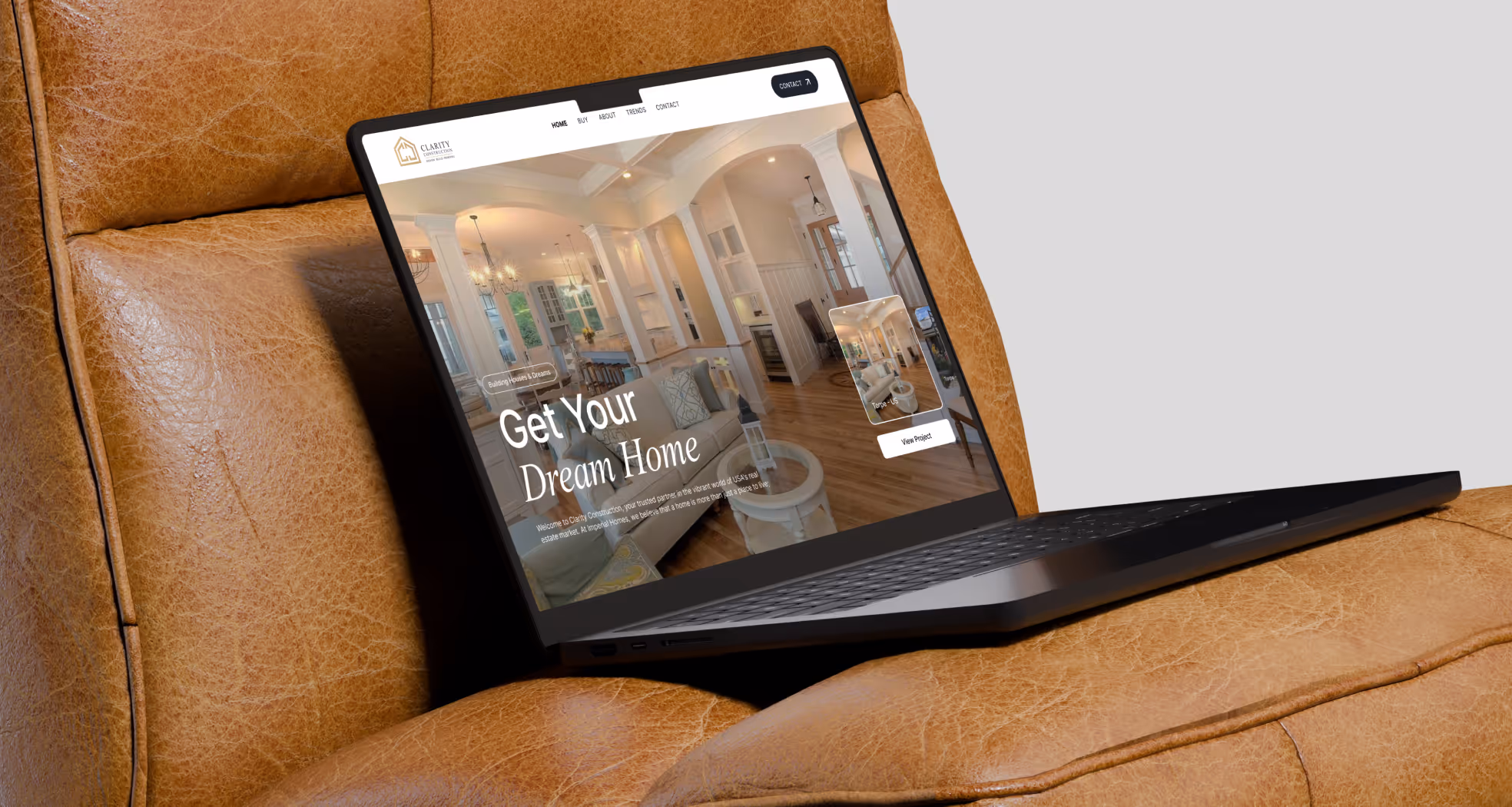 Open laptop displaying a home construction website with the headline Get Your Dream Home on a brown leather chair.