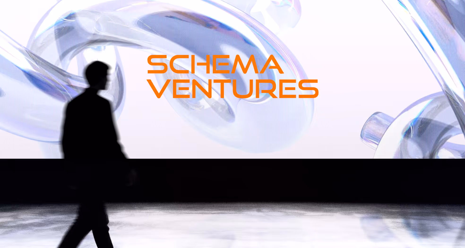 Silhouette of a person walking in front of a large screen displaying 'SCHEMA VENTURES' in orange text with a translucent abstract background.