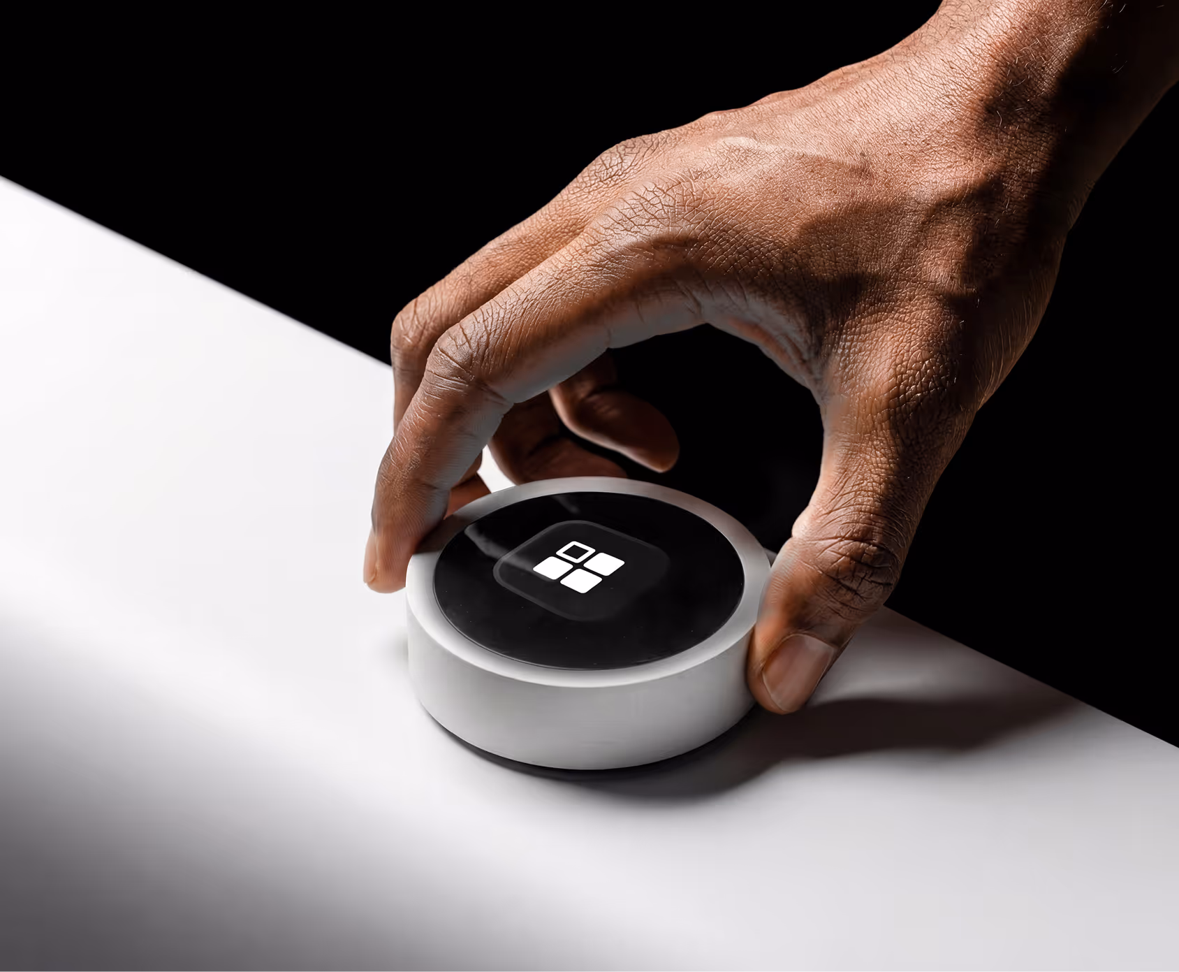 Hand picking up a white smart speaker with a black top and four white square icons.