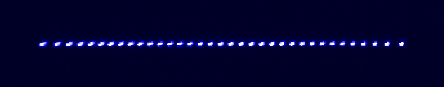 A microscopic image of a linear chain of 35 ytterbium ions that form the quantum register in the current configuration of the IonQ Forte system. The central 31 qubits are imaged onto 31 individual detection channels for fast quantum state measurement. For scale, the separation between ions in this chain is roughly 3μm (roughly 100μm from side to side).