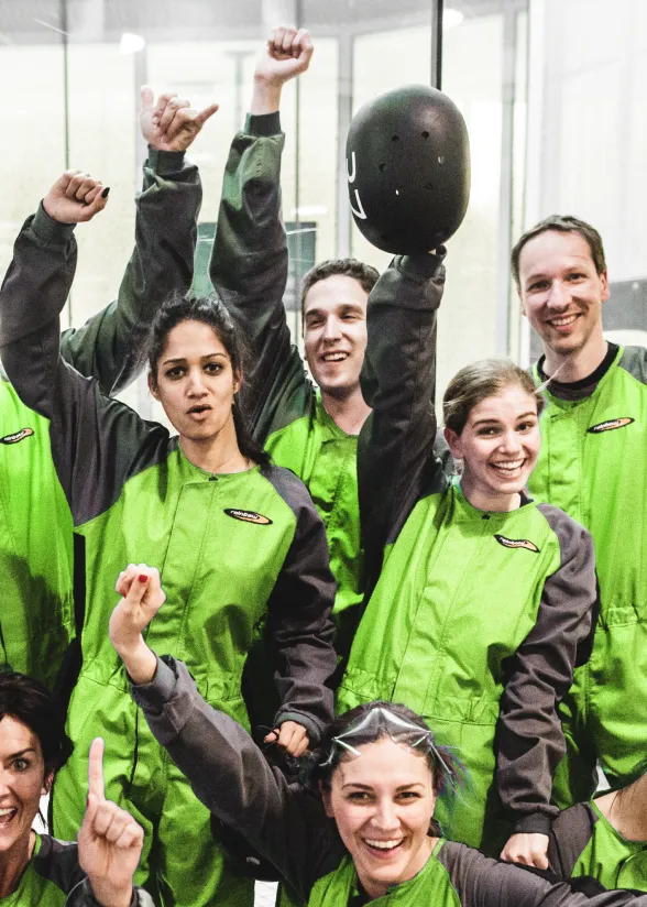 Group of people in green suits celebrating after indoor skydiving.